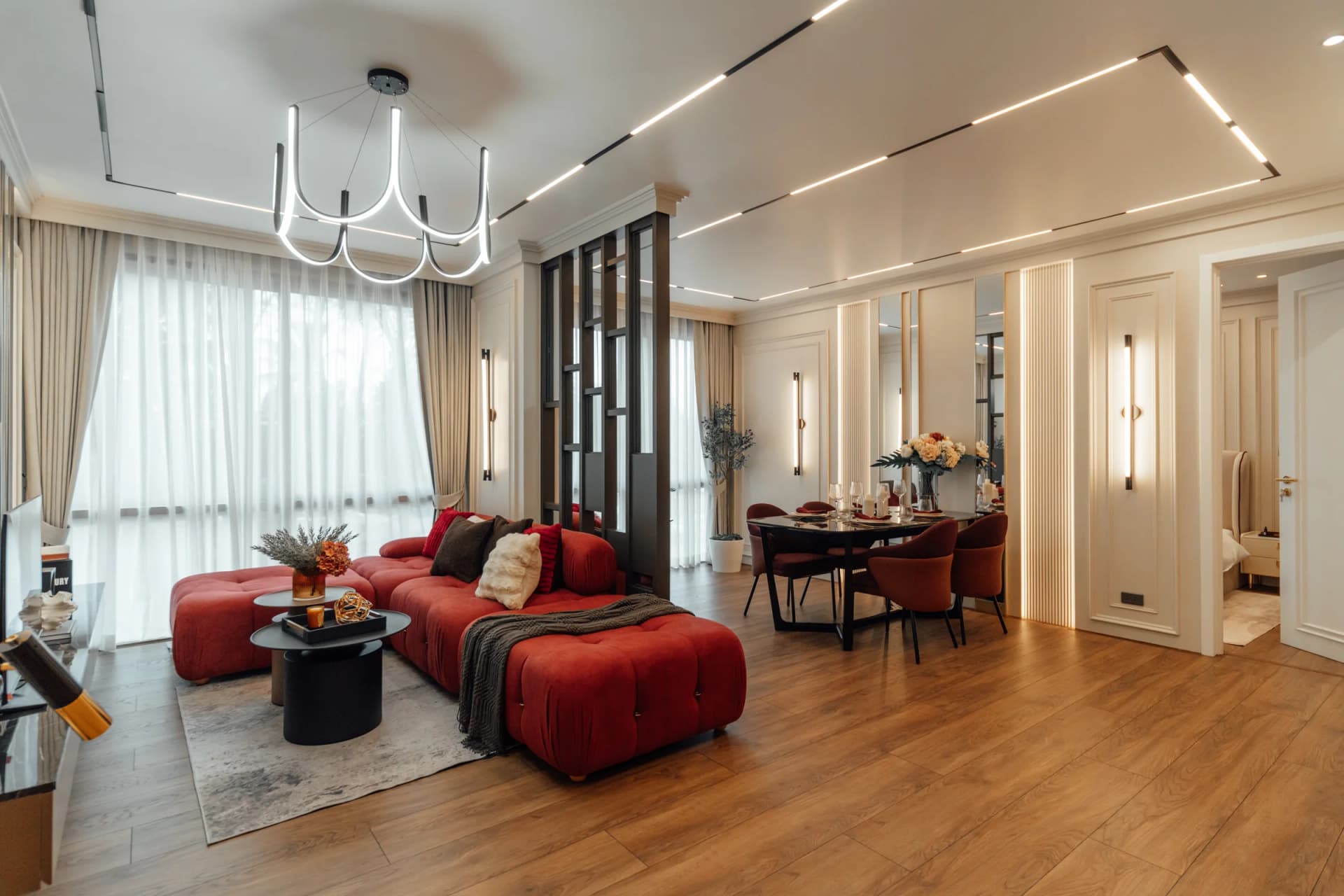 Apartamento piloto, foto real: el salón con el sofá rojo, la lámpara de anillo y la mesa de comedor junto a la ventana